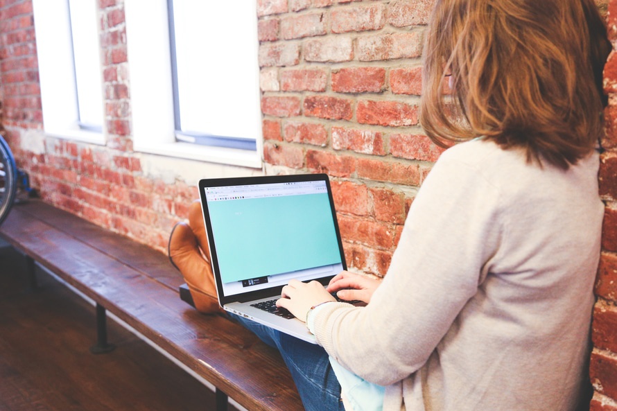 Woman on laptop against a brick wall